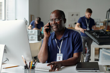 Aufkleber - Experienced technician of repair service looking at computer screen while sitting by workplace and speaking to client on smartphone