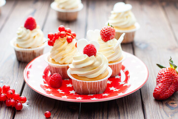 Wall Mural - Vanilla cupcakes decorated with fresh strawberry, raspberry and red currant on rustic wooden background