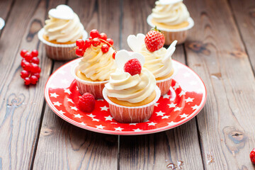Wall Mural - Vanilla cupcakes decorated with fresh strawberry, raspberry and red currant on rustic wooden background