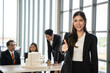 © Bavorndej - Asian businesswoman gives a thumbs up to the camera with an attractive smile. She stands with team at the office.