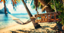 Wooden CHILL Sign Hanging On A Hammock Between Palm Trees On A Tropical Beach With A Serene Ocean View, Epitomizing Relaxation And A Laid-back Lifestyle