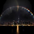 Regenbogen bei Nacht über einer Stadt am Meer