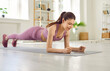 © Studio Romantic - Happy beautiful smiling fit young woman in sportswear having fitness workout at home, using modern fitness app on her cellular phone and doing plank exercise on yoga mat on floor