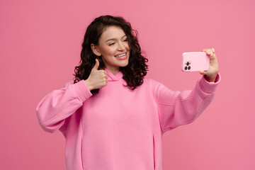 Wall Mural - happy smiling woman in pink hoodie posing on pink studio background holding smartphone