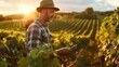 Farmer with tablet during sunset in lush vineyard landscape.
