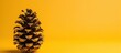 A single pine cone is positioned on top of a bright yellow table, standing out against the vivid background. The contrast between the textured pine cone and the smooth surface of the table creates a