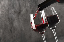 Pouring Red Wine Into Glass Against Grey Background, Closeup. Space For Text