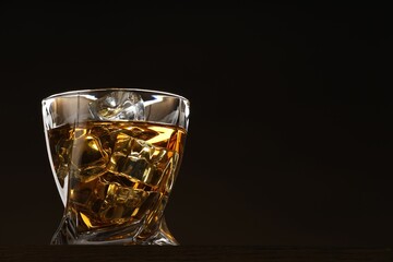 Sticker - Whiskey with ice cubes in glass on table against black background. Space for text