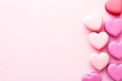A collection of heart-shaped cookies neatly arranged on a pink background. Cookies of different sizes and decorated with colorful icing. Some of the cookies have sprinkles that 