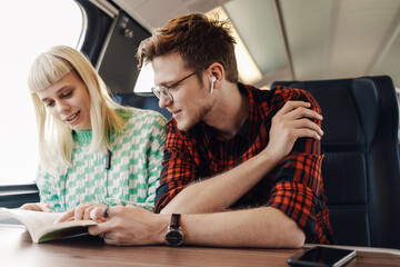 Wall Mural - A young travelers sitting in a train next to a window and reading a book.