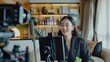 © Matcha_09 - Asian businesswoman working from home live video interaction with customers using camera device vlogging selling make up products,