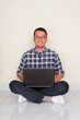 © KrishnaTedjo - Adult Asian man sitting crossed leg with laptop on his lap showing happy expression
