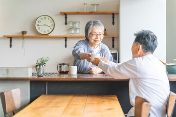 Canvas Print - キッチンからコーヒーを渡すシニアの女性・妻・奥さんコーヒーを受け取るシニアの男性・夫
