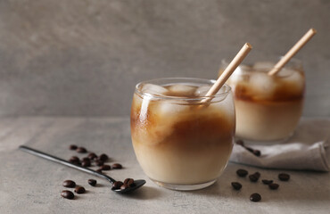 Wall Mural - Refreshing iced coffee with milk in glasses, beans and spoon on gray table, closeup. Space for text