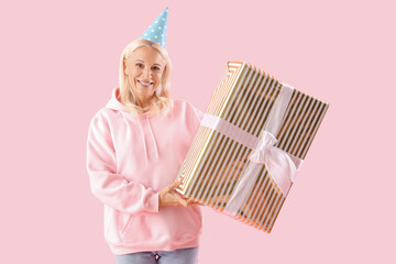 Poster - Happy mature woman in party hat with big gift box on pink background