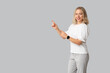 © Pixel-Shot - Pretty young woman with modern smartwatch pointing at something on grey background