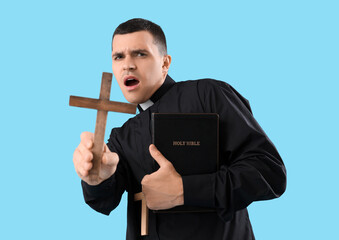 Wall Mural - Shocked young priest with Holy Bible and crosses on blue background