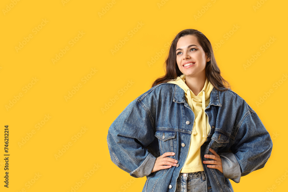 Pretty young woman in stylish denim jacket on yellow background