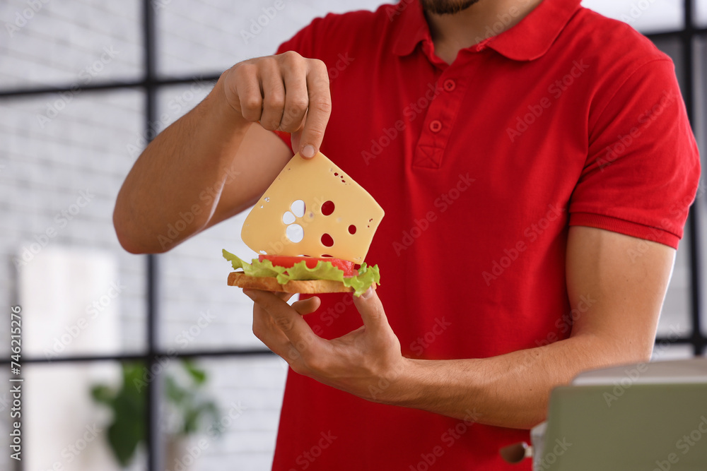 Young man making delicious sandwich with crispy toasts in kitchen, closeup