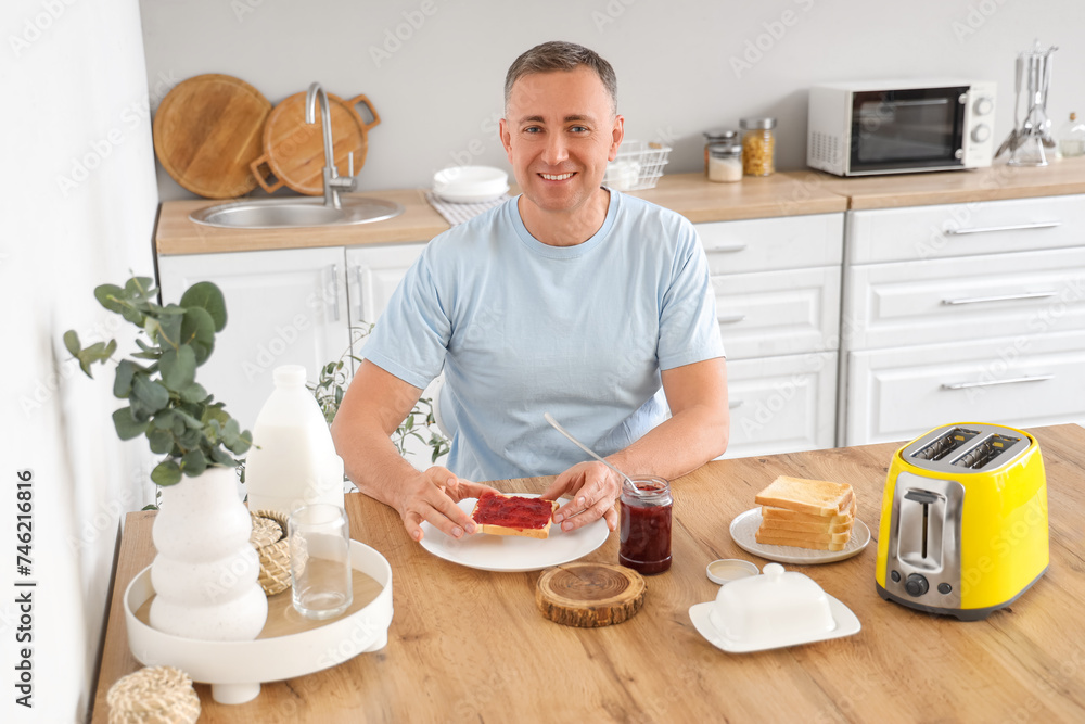 Middle-aged man having sweet jam toasts for breakfast in kitchen