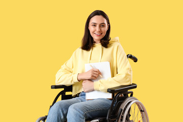 Poster - Happy young woman in wheelchair with notebook on yellow background