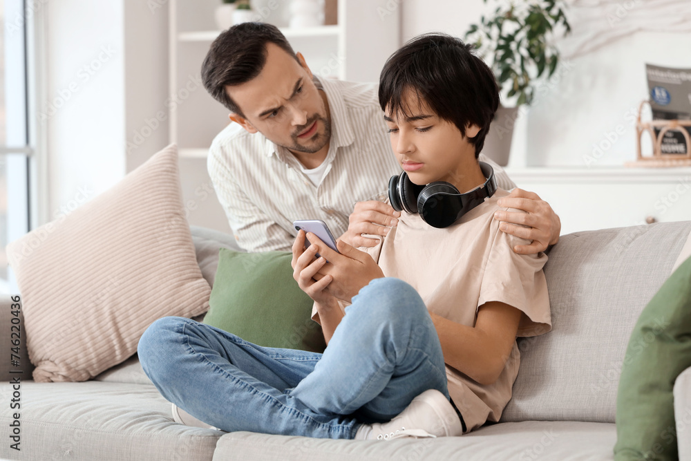 Teenage boy with his upset father using mobile phone at home. Family problem concept