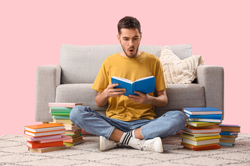 Poster - Shocked young man reading book near sofa on pink background