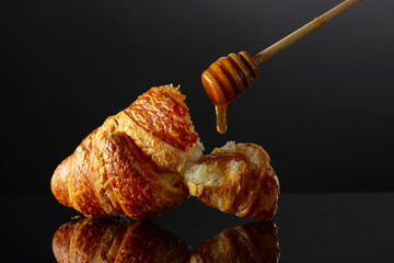 Sticker - Fresh baked croissant with honey on a black reflective background.