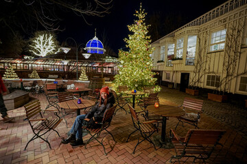 Christmas amusement park. A woman sits in an empty street cafe in the evening.