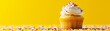 : A creative and enticing food composition featuring a butter cupcake muffin with creamy frosting and colorful sprinkles, set against a vibrant yellow background. 