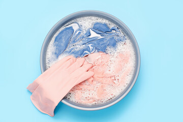 Colorful clothes washed with basin with soap bubbles close-up on a blue background, top view.