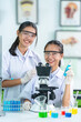 © Nutchapong Wuttisak - 2 female students, Faculty of Medicine Standing at work and conducting research on medicines related to chemical cells using a microscope. There are beakers and test tubes in the science lab.