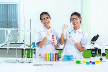 Two Asian female WHO scientists, both doctors, stand holding test tubes and chemicals in a biological lab for use as vaccines and medicines to treat COVID and other global pandemics in science.