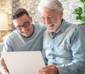 Sticker - Smiling experienced young boy with laptop teaching and showing new computer technology to his old grandfather for surfing internet, shopping online, managing bank. Old man learns to use the computer