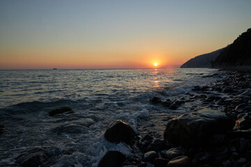 Wall Mural - Sun dips below horizon, rocky coastline, nature beauty in serene tranquility. Waves gently lap against shore, while silhouetted cliffs stand majestically against dusky sky