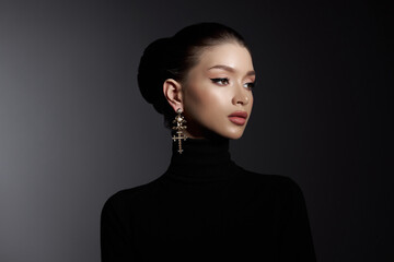 Wall Mural - Woman with elegant makeup and a cross earring poses in a black turtleneck, exuding sophistication