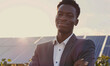 Portrait of young black African businessman and sustainable business entrepreneur staring at the camera with solar farm and solar panels in background. Isolated shot with bokeh, sunny, bright, outside