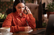 © Andrii Lysenko - Young freelancer woman taking notes in a notepad, calling on the phone while working on a computer in a cafe.