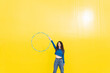 © VISTA by Westend61 - Woman playing with hula hoop standing against yellow background