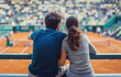 © Bonsales - Young couple looks at tennis players performing during match. Man and woman in love feel mix of awe and excitement observing fast-paced action