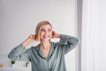 Sticker - Photo of young girlfriend wearing grey comfortable pajama brushing hair looking far away in window chilling at light interior home indoors