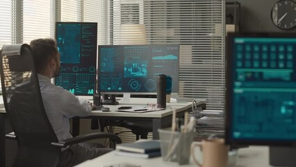 Back view shot of male professional cybersecurity officers sitting at desks by multiple computer displays and monitoring confidential data information