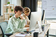 © LIGHTFIELD STUDIOS - Curly-haired man concentrating on retouching work near coworker in a startup office space