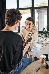 Wall Mural - happy young professionals with laptop and smartphone discussing startup project, men in their 20s