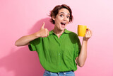 Fototapeta Panele - Photo portrait of attractive young woman hold coffee mug show thumb up dressed stylish green clothes isolated on pink color background
