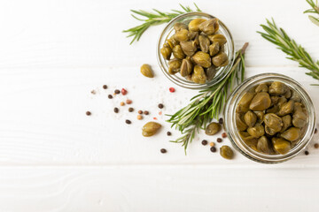 Capers in a bowl on a wooden kitchen table. Capers with sea salt and rosemary. Pickled capers.Mediterranean cuisine ingredient. Organic spices and seasonings. Copy space.