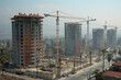 City with construction cranes towering overhead, symbolizing the rising costs of construction materials and housing, exacerbating affordability issues and contributing to inflationary pressures