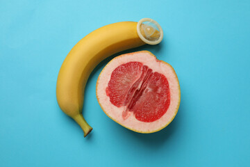 Wall Mural - Banana with condom and half of grapefruit on light blue background, flat lay. Safe sex concept