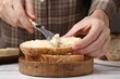 Woman spreading butter onto bread at white wooden table, closeup