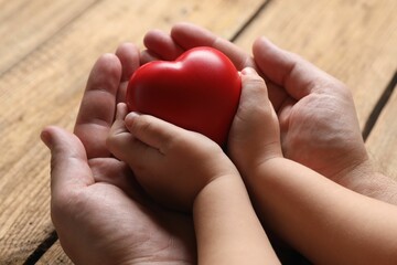 Wall Mural - Father and his child holding red decorative heart at wooden table, closeup